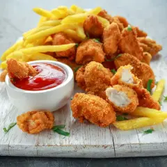 Chrupiące, złociste domowe nuggetsy jak z McDonalda, podane z frytkami i ketchupem na białej desce.