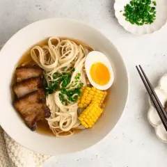 A miseczce aromatyczny shoyu ramen z makaronem, plastrami boczku, jajkiem na pół, kukurydzą i szczypiorkiem.