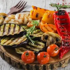 Co przygotować na grilla ze znajomymi? Grillowane bakłażany, papryki, pieczarki, pomidorki i marchewka na drewnianej desce.