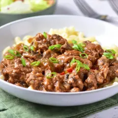 Pyszny przepis na strogonowa z wieprzowiny z pieczarkami i ogórkiem kiszonym, podany z makaronem i posypany szczypiorkiem.