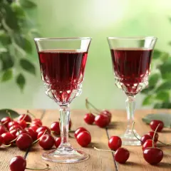 Dwa kieliszki z rubinową, szybką nalewką z wiśni na spirytusie, otoczone świeżymi wiśniami na drewnianym stole.