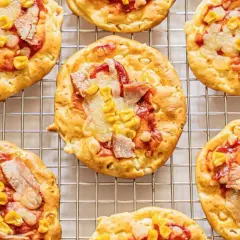 Mini pizze z serka wiejskiego, z kukurydzą i kawałkami mięsa, ułożone na metalowej kratce.