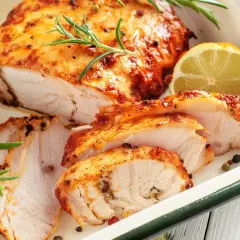 Soczysty, pieczony filet z indyka, pokrojony w plastry, z gałązkami rozmarynu i plasterkiem cytryny.