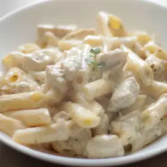 Penne z kurczakiem w kremowym sosie śmietanowym, udekorowane gałązką ziół. Pyszne danie gotowe do podania.