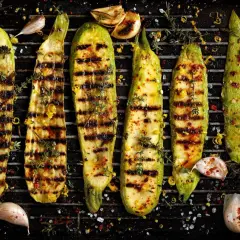 Pyszna cukinia z grilla, doprawiona czosnkiem, tymiankiem i płatkami chili, leży na ruszcie.