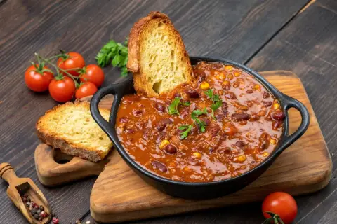 Pyszne dania na obiad: aromatyczne chili con carne z fasolą i kukurydzą, podane z chrupiącym pieczywem i świeżymi pomidorkami.
