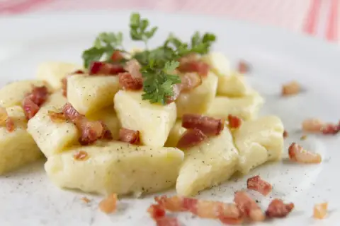 Kopytka z chrupiącym boczkiem i natką pietruszki, posypane pieprzem. Pyszne danie, które zadowoli każdego smakosza.