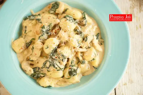 Pyszne gnocchi z kurczakiem i szpinakiem w kremowym sosie, posypane parmezanem. Danie wygląda apetycznie i zachęca do spróbowania.