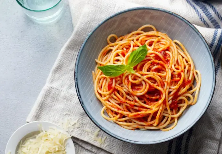 Misternie ułożone spaghetti z sosem pomidorowym i listkiem bazylii. Obok miseczka z tartym parmezanem. Idealne pytanie: jakie przyprawy do spaghetti?