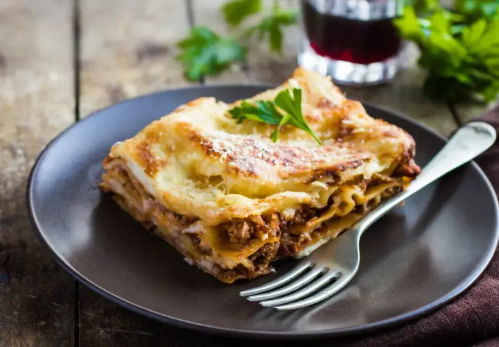 Pyszny kawałek lasagne z mięsem mielonym, idealny na prosty obiad. Posypana parmezanem i udekorowana natką pietruszki.