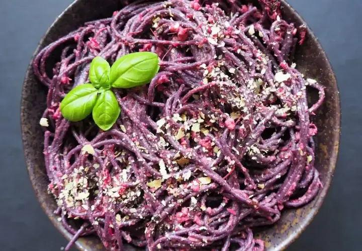 Fioletowy makaron z pesto ze słoika, posypany orzechami i udekorowany listkiem bazylii.