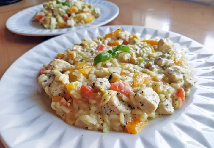 Szybkie risotto z warzywami i kurczakiem, udekorowane listkiem bazylii. Pyszne i kolorowe danie na talerzu.