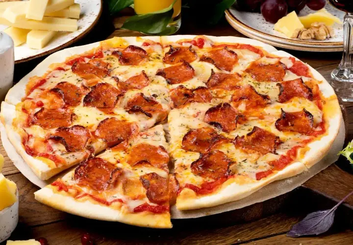 Pyszna pizza pepperoni z ciągnącym serem, obok serowe dodatki do pizzy, winogrona i kieliszek czerwonego wina.
