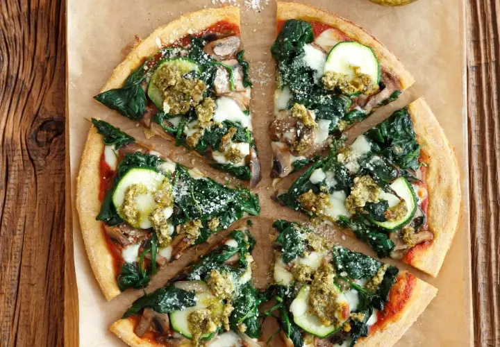 Pyszna pizza ze szpinakiem, cukinią i grzybami, polana sosem pesto.