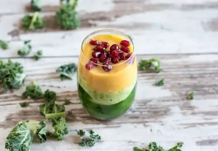Warstwowy koktajl z jarmużu, mango i granatu, ozdobiony pestkami granatu.
