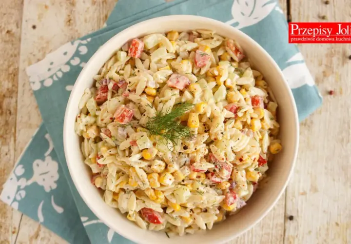 Pyszna sałatka z makaronem orzo, szynką, kukurydzą i ogórkiem, udekorowana koperkiem. Idealna na letnie dni.