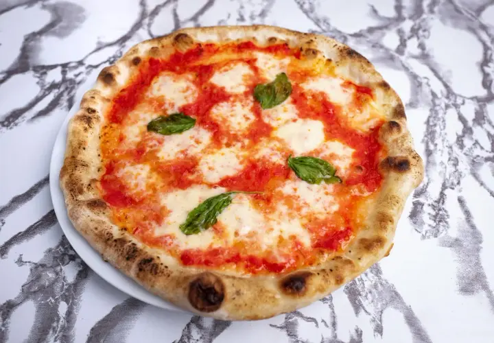 Pyszne ciasto na pizzę neapolitańską z pomidorami, mozzarellą i bazylią, idealne na letni wieczór.