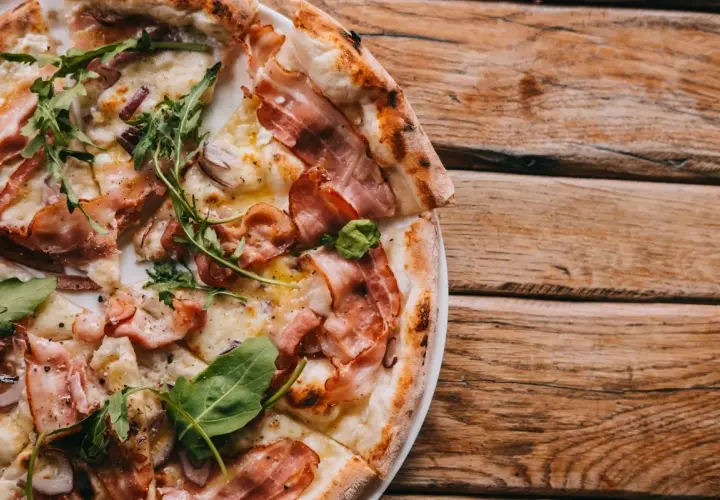 Pyszna pizza carbonara z chrupiącym boczkiem i rukolą, podana na drewnianym blacie.