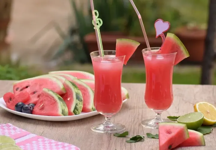 Orzeźwiająca lemoniada arbuzowa z plasterkami arbuza, cytryny i limonki na drewnianym stole.