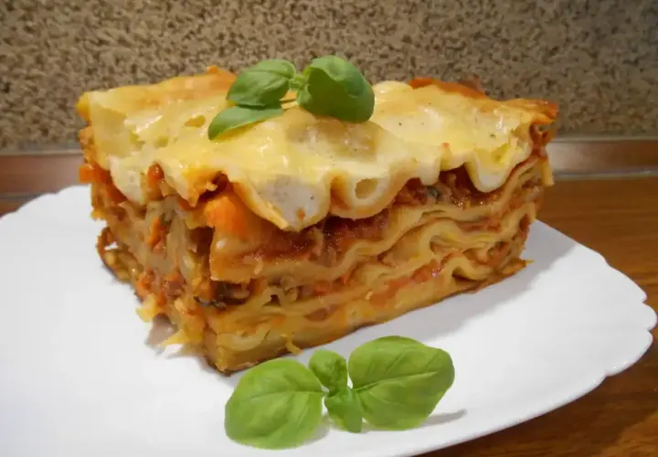 Pyszna, wielowarstwowa lasagne z sosem pomidorowym i serem, ozdobiona listkami bazylii. Idealna inspiracja, jak zrobić lasagne.