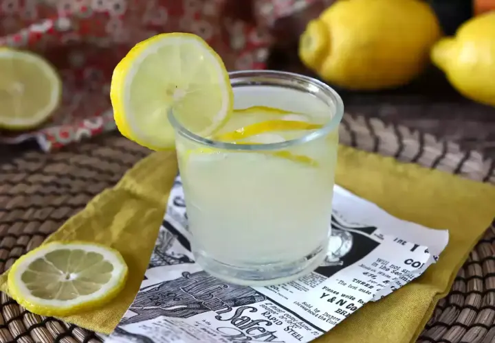 Orzeźwiający drink z limoncello, ozdobiony plasterkiem cytryny, na tle cytryn i wzorzystej tkaniny.