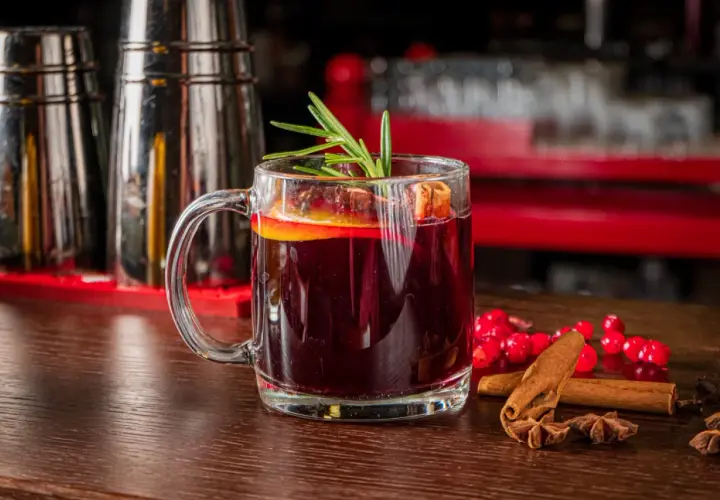 Aromatyczny grog z pomarańczą i rozmarynem, ozdobiony laskami cynamonu i gwiazdkami anyżu, kusi na drewnianym blacie.
