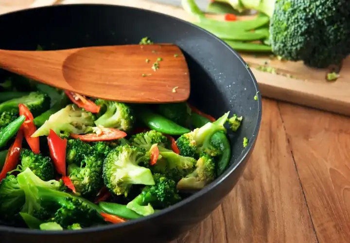 Brokuły, groszek cukrowy i papryczka chili w woku, gotowe do stir fry. Drewniana łopatka miesza warzywa.