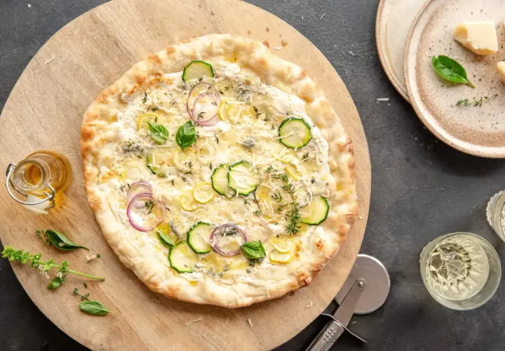 Pyszna pizza bianca z cukinią, cebulą i cytryną, podana na drewnianej desce.