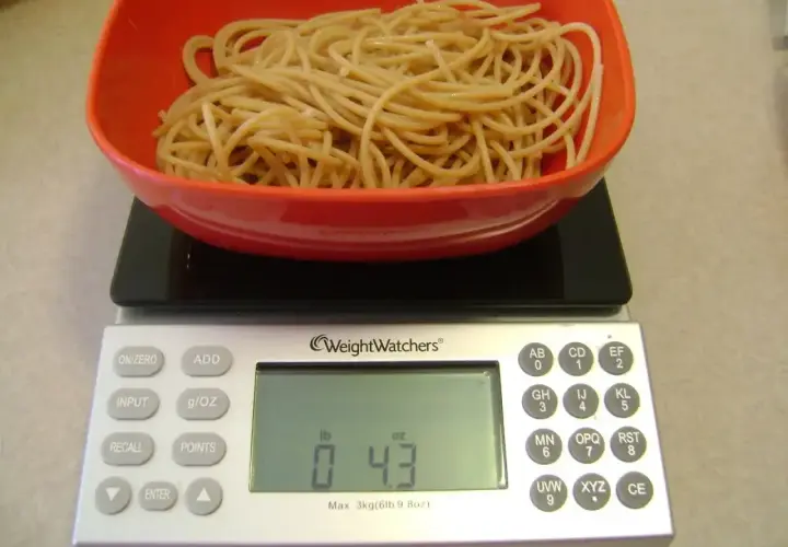 Porcja makaronu w czerwonej misce na wadze cyfrowej. Waga pokazuje 0.43 funta, co pomaga w ustaleniu, jak liczyć kalorie makaronu.