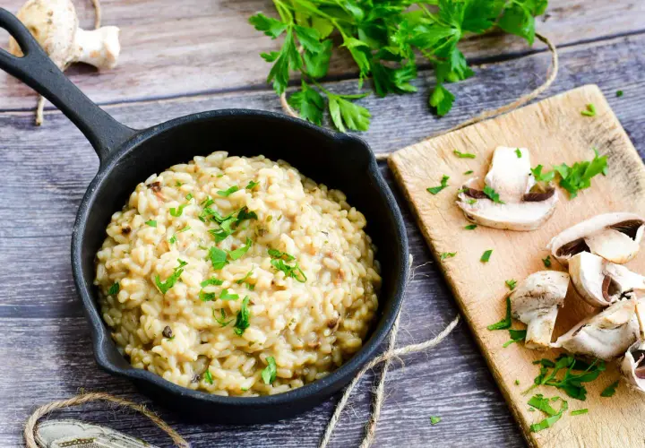 Kremowe risotto z grzybami i natką pietruszki w czarnej patelni.