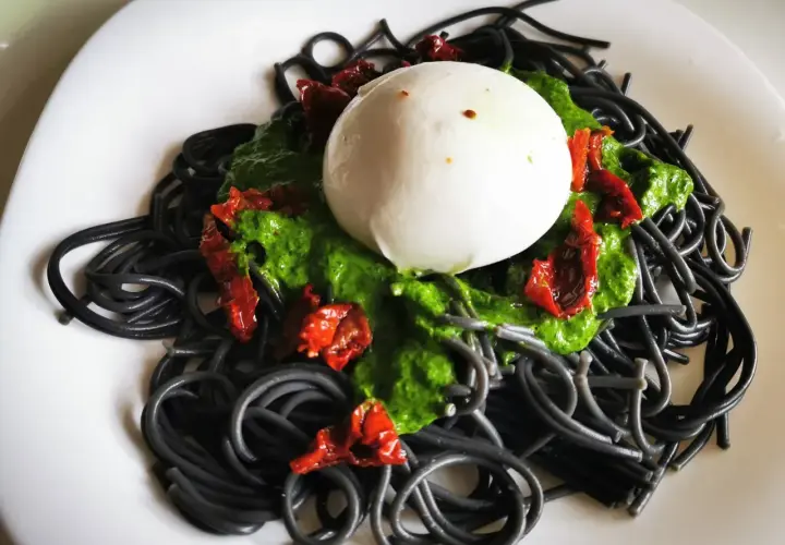 Czarny makaron z zielonym pesto, suszonymi pomidorami i kulką mozzarelli. Pyszne danie, które zachwyca wyglądem i smakiem.
