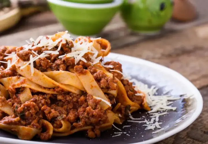 Pyszne tagliatelle z sosem bolognese, posypane parmezanem. Idealne danie, gdy zastanawiasz się, ile smażyć mięso mielone do spaghetti.