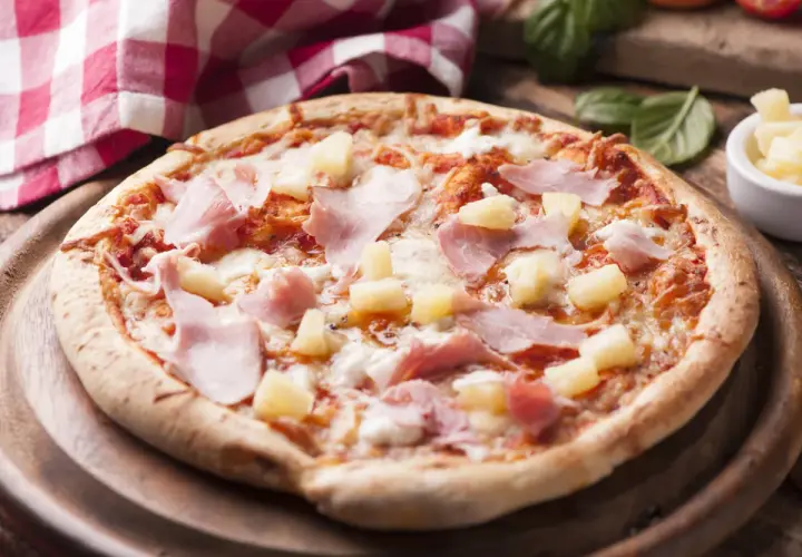 Apetyczna pizza z ananasem i szynką, polana ciągnącym się serem, na drewnianej desce.