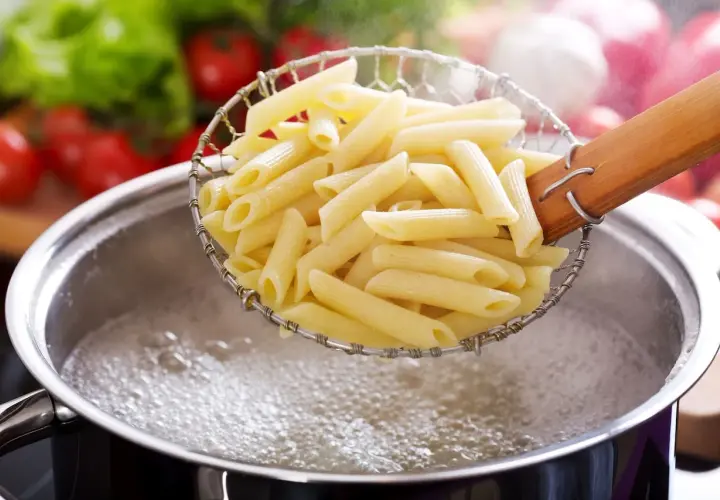 Penne w cedzaku, gotowe do podania, idealnie ugotowane makaron al dente. W tle pomidory i sałata.