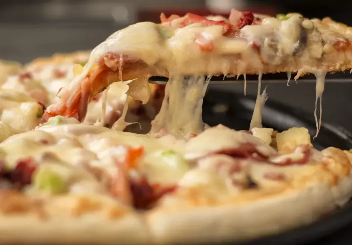 Gorąca, ciągnąca się pizza mrożona z serem, szynką i ananasem. Kawałek pizzy jest podnoszony, odsłaniając roztopiony ser.