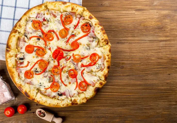 Apetyczna pizza capricciosa z pomidorkami, papryką i serem na drewnianym blacie.