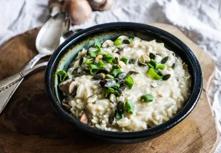 Aksamitne risotto z pieczarkami, posypane pestkami dyni i szczypiorkiem, czeka na talerzu.