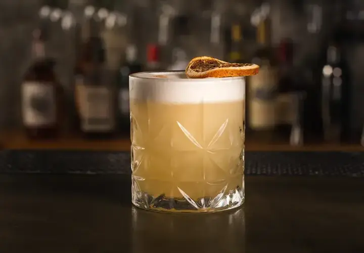 Klasyczny whisky sour przepis: orzeźwiający koktajl z pianką i plasterkiem suszonej pomarańczy.
