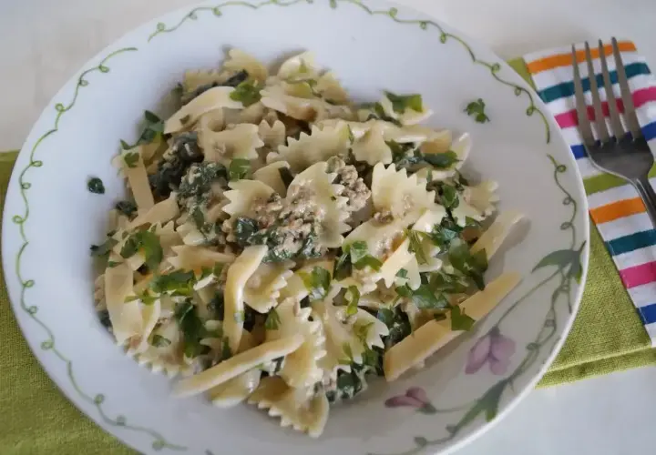 Pyszny makaron farfalle z tuńczykiem i szpinakiem, posypany świeżą natką pietruszki.