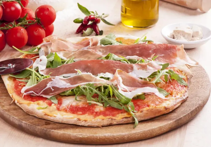 Pyszna pizza prosciutto z rukolą, pomidorami i oliwą z oliwek. Idealna na włoską ucztę.