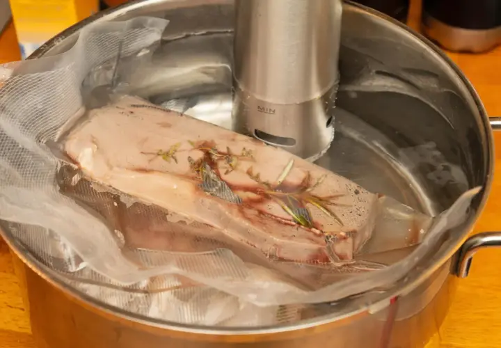 Mięso w woreczku z ziołami, zanurzone w wodzie z cyrkulatorem sous vide.