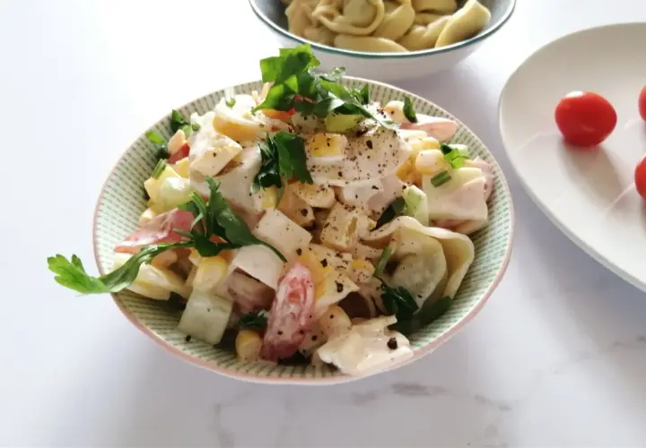 Pyszna sałatka z tortellini, jajka, kukurydzy i pomidorów, udekorowana natką pietruszki. Idealna na letnie dni, to najlepsza sałatka z tortellini.