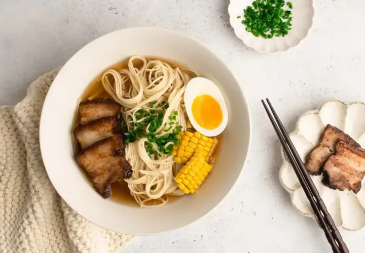 A miseczce aromatyczny shoyu ramen z makaronem, plastrami boczku, jajkiem na pół, kukurydzą i szczypiorkiem.