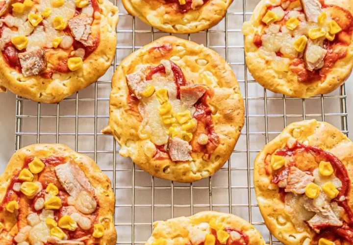 Mini pizze z serka wiejskiego, z kukurydzą i kawałkami mięsa, ułożone na metalowej kratce.