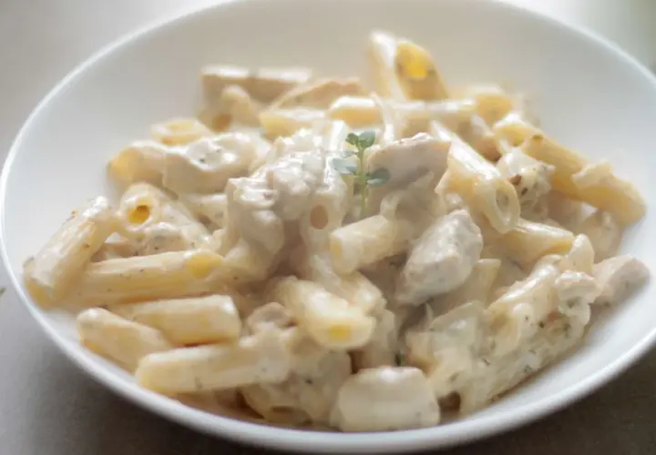 Penne z kurczakiem w kremowym sosie śmietanowym, udekorowane gałązką ziół. Pyszne danie gotowe do podania.