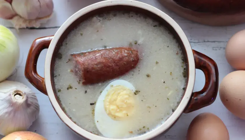 Aromaticzny żurek z kiełbasą i jajkiem, przygotowany na bazie domowego zakwasu na żurek. Obok czosnek, cebula i jajka.