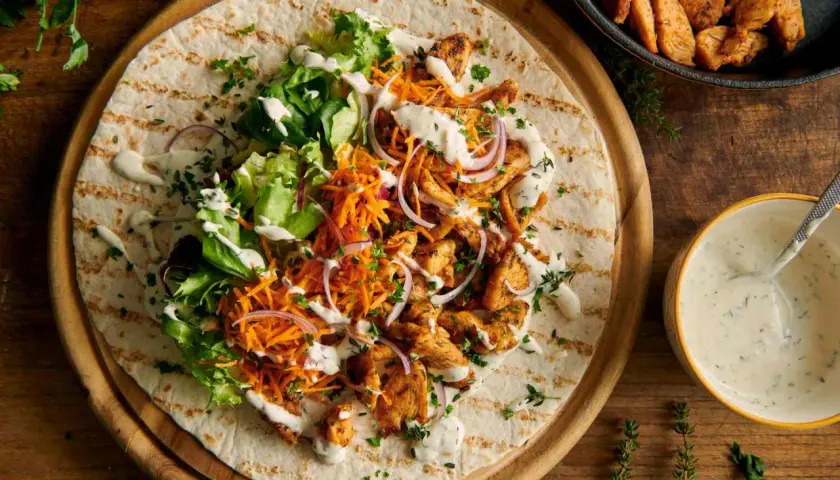 Pyszny kebab na tortilli z kurczakiem, sałatą, marchewką i cebulą, polany kremowym sosem do kebaba.