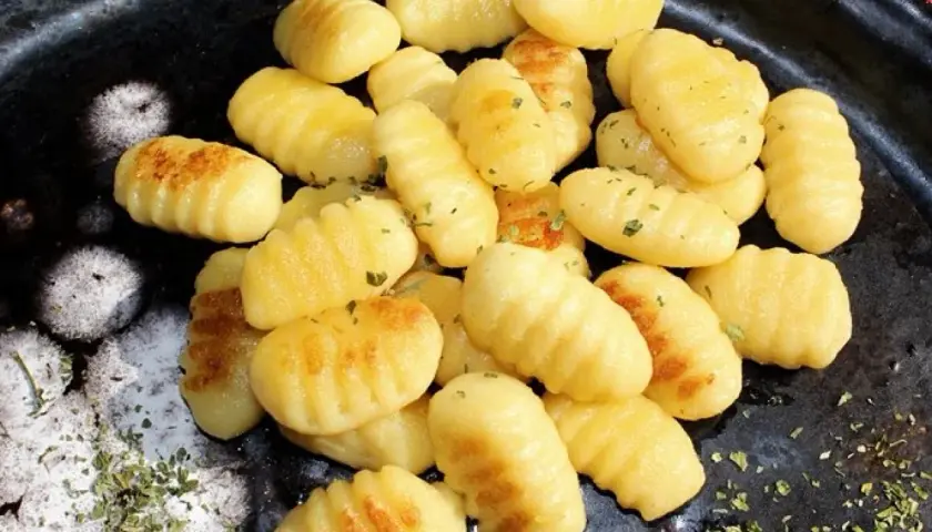Złociste, domowe **makaron gnocchi** z ziołami, ułożone na ciemnym talerzu.