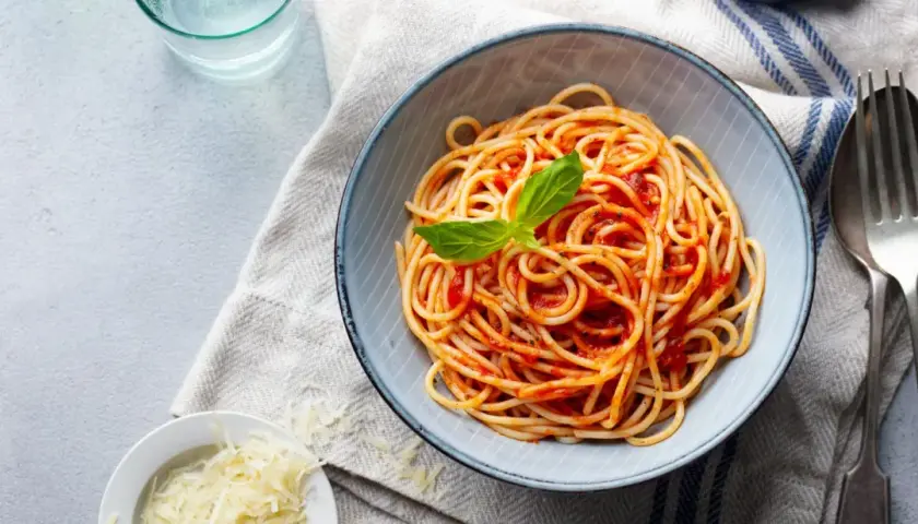 Misternie ułożone spaghetti z sosem pomidorowym i listkiem bazylii. Obok miseczka z tartym parmezanem. Idealne pytanie: jakie przyprawy do spaghetti?