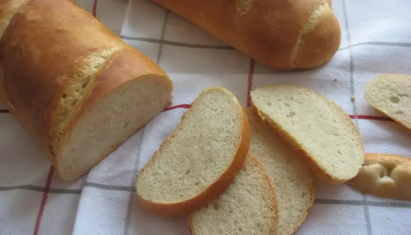 Chleb pszenny na zakwasie, pokrojony w kromki, leży na kratkowanym obrusie. Idealny do śniadania.